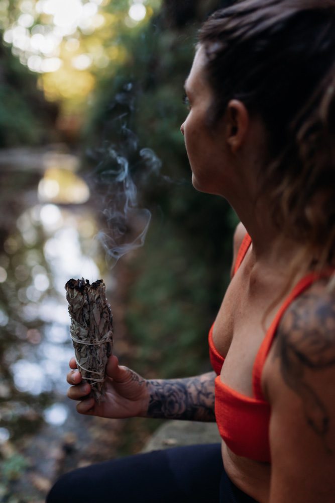 Megan Zechel standing in the forest holding a bundle of sage, a quiet moment to process emotions
